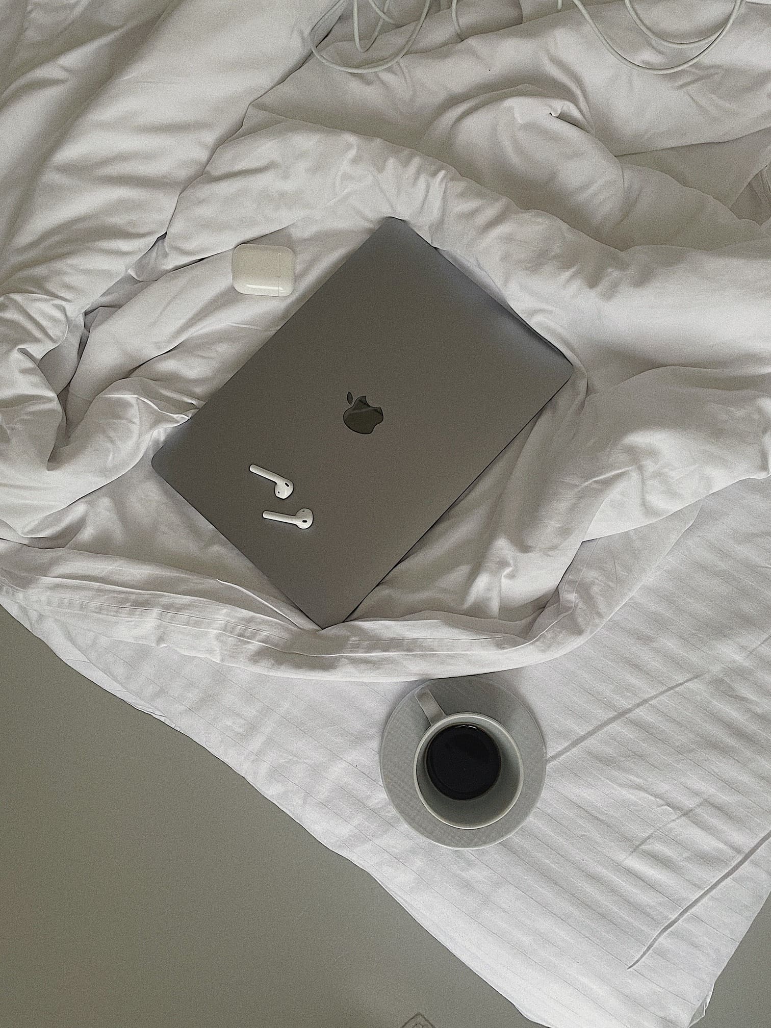 laptop and airpod on bed with white sheets